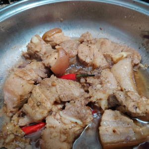 Cooked pork pieces in a soy-free adobo style with garlic, bay leaves, and peppercorns in a pan